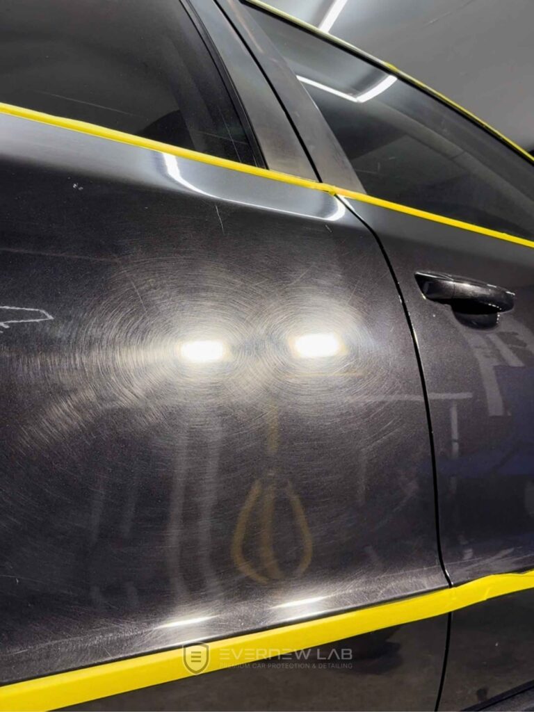 Close-up of heavy swirl marks on a black Mercedes-Benz door panel before professional paint correction at EverNew Lab, Sydney.