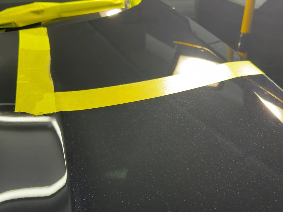 Masking tape marking a test section on a black car bonnet during paint correction