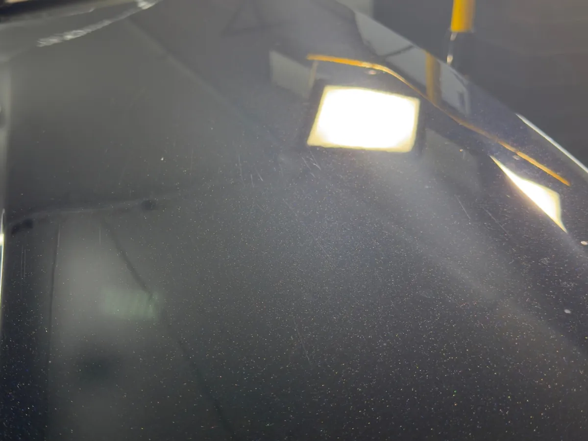 Fine scratches and swirl marks on black car paint under an inspection light before paint correction